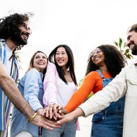 diverse-group-of-cheerful-millennial-friends-standing-together-stacking-hands-in-the-street